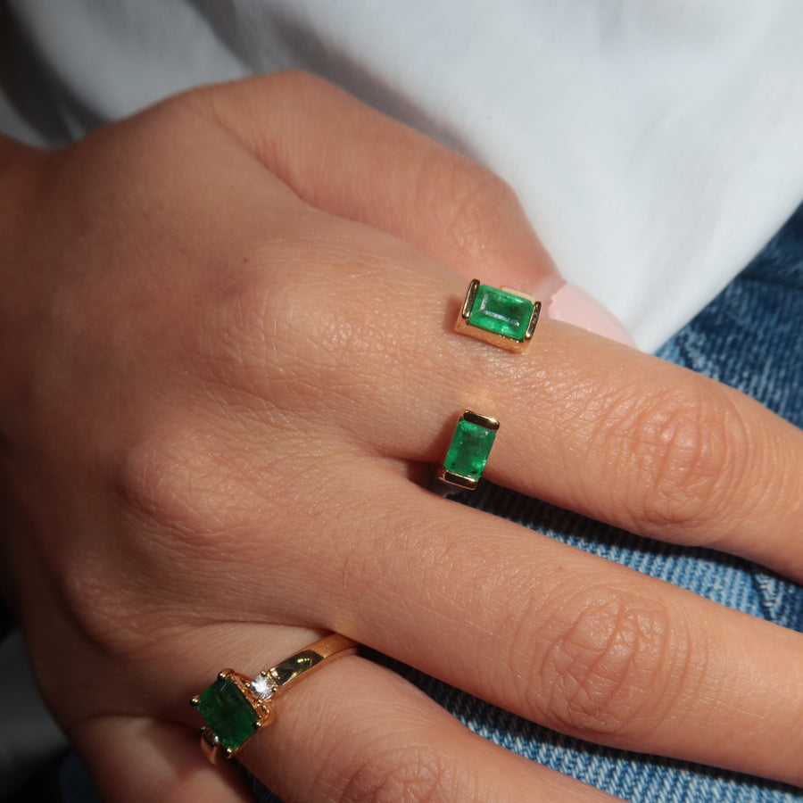 Hand wearing two natural zambian emerald green gemstones on gold rings on a blue denim background