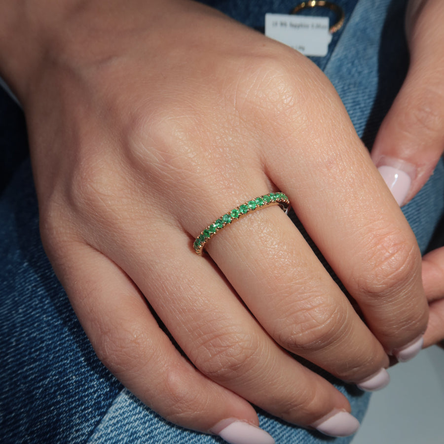 Hand wearing a Zambian emerald band ring on a blue denim background