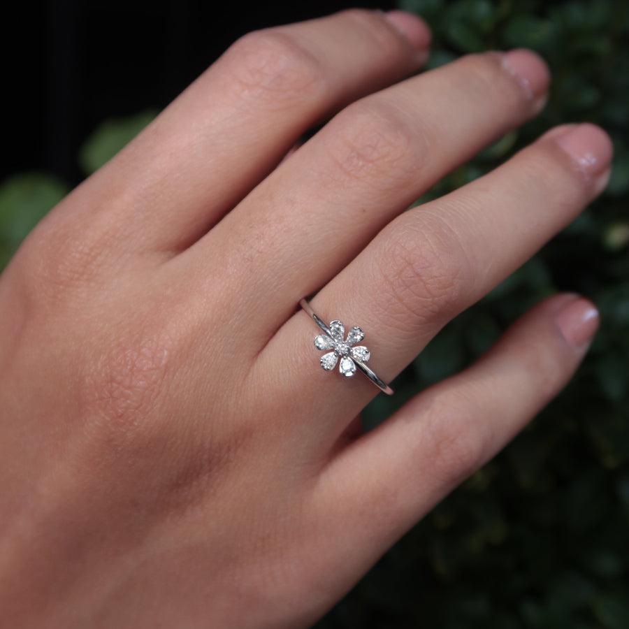 Hand wearing a white gold ring with a floral design against a blurred green background