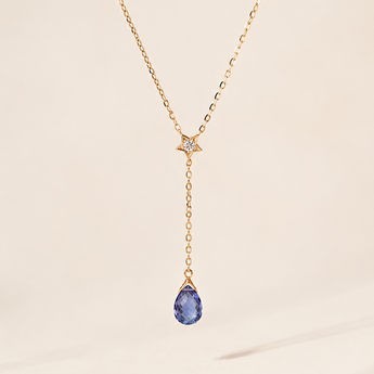 Gold necklace with a blue briolette teardrop pendant on a beige background
