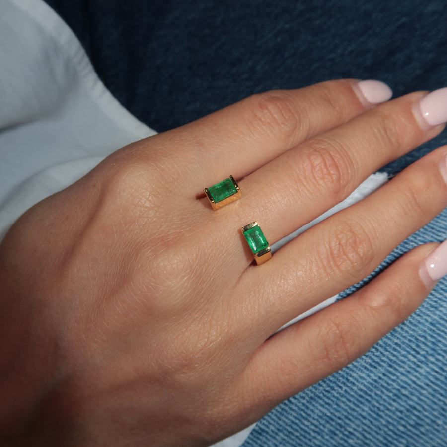 Hand wearing a gold ring with Zambian emerald gemstones against a blue fabric background