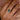 Hand wearing a 18k yellow gold zambian emerald and white sapphires gemstone ring on a soft pink fabric background