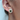 Close-up of an ear wearing a gold earring with a green gemstone on a light background