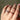 Hand wearing a ring with multicolored gemstones against a neutral background
