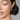 A close-up image of a woman wearing a white gold diamond earring with a round and baguette diamond design.