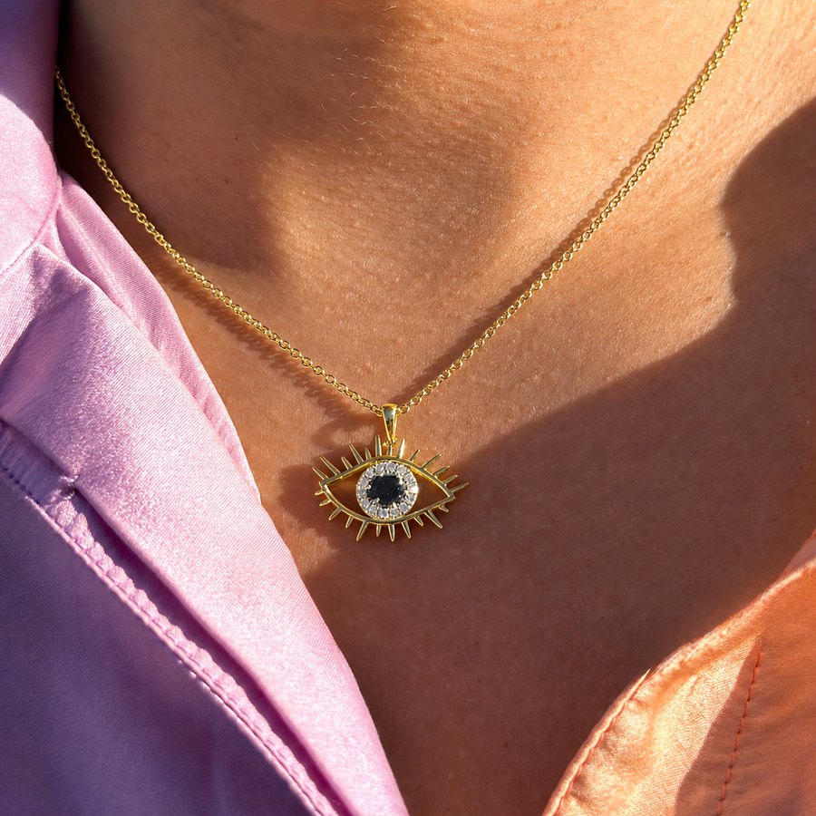 Gold necklace with an eye-shaped pendant worn by a person in a pink shirt.