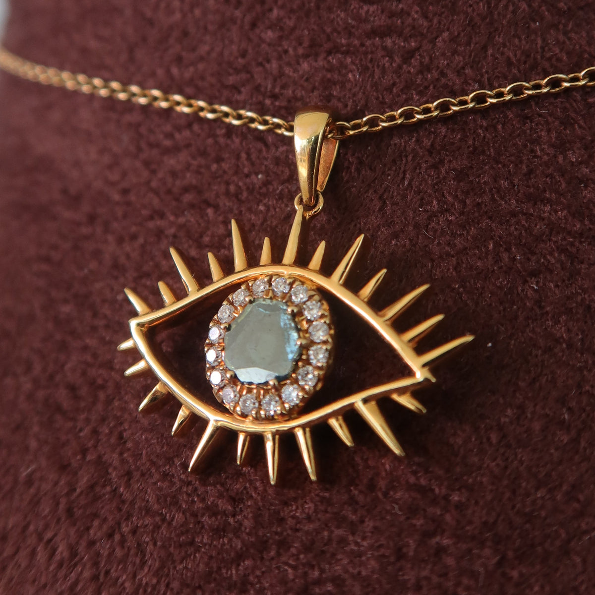 Gold pendant with eye design on a chain against a brown fabric background - Psylish