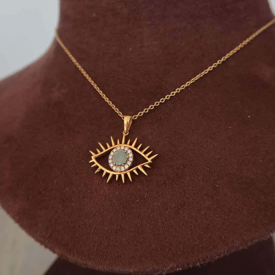 Gold necklace with an eye-shaped pendant on a brown velvet stand.