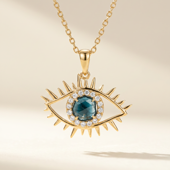 Gold necklace with an eye-shaped pendant featuring a blue gemstone on a beige background